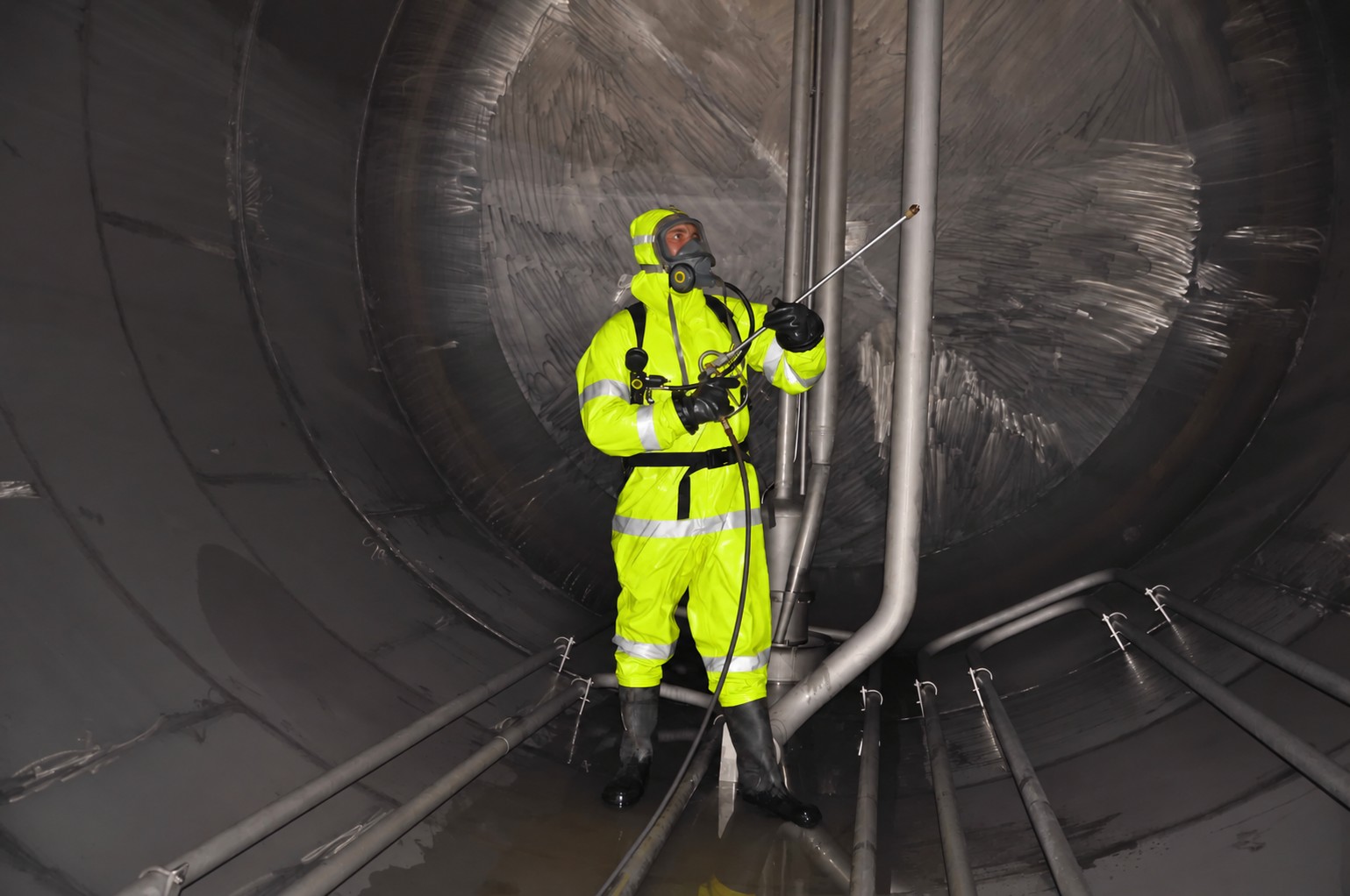 Worker in a fluorescent yellow suit with reflective bands inside an industrial tank; suit digitally edited